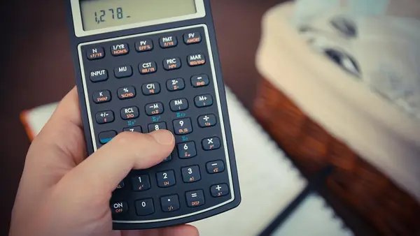 Mano usando una calculadora junto a un cuaderno