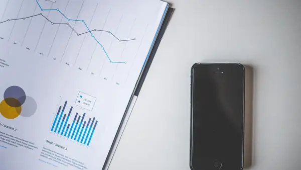 Informe impreso con gráficos de líneas y de barras junto a un teléfono sobre un escritorio